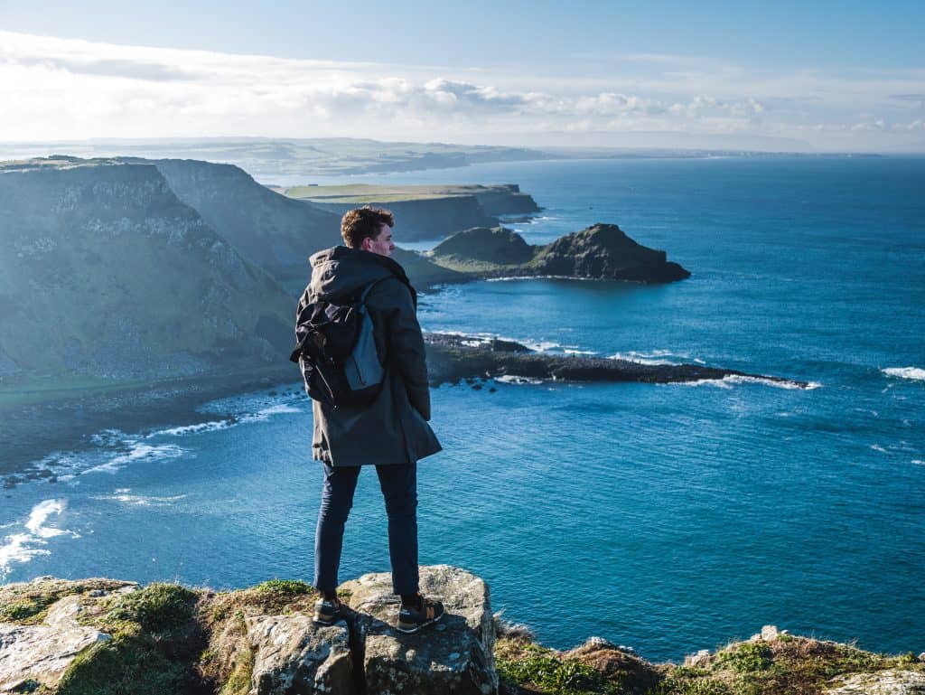 man standing on cliff looking on clear blue sea during daytime